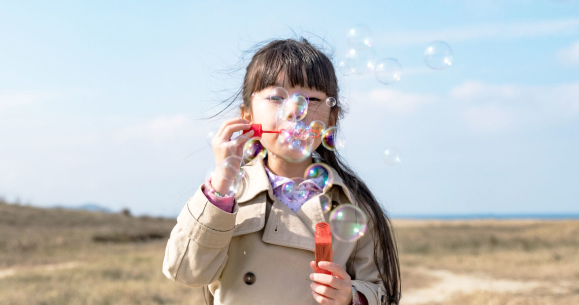 girl blowing bubbles wearing coat